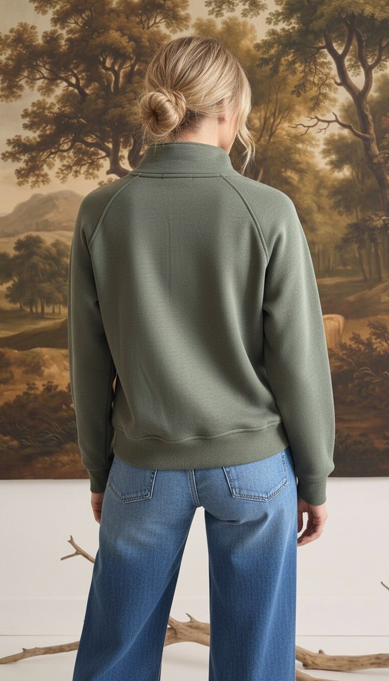Back view of a woman wearing a graced olive green half zip mock neck pullover with blue jeans
