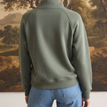 Back view of a woman wearing a graced olive green half zip mock neck pullover with blue jeans