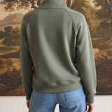 Back view of a woman wearing a graced olive green half zip mock neck pullover with blue jeans