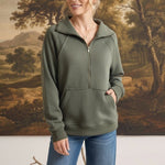 Woman wearing a graced olive green half zip mock neck pullover with a front kangaroo pocket and blue jeans