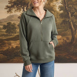 Woman wearing a graced olive green half zip mock neck pullover with a front kangaroo pocket and blue jeans