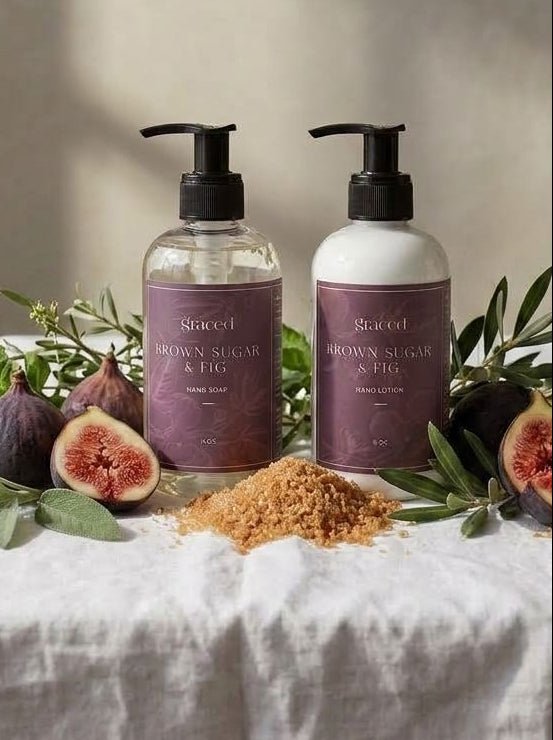 Two pump bottles of Swocet Brown Sugar & Honey body wash and hand wash arranged on a white linen tablecloth with fresh figs, green leaves, and brown sugar piles, against a textured beige wall with soft window light.