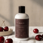 Graced Door County Cherry hand lotion in a small bottle, part of the Bath + Body lotion collection, featuring cherry scent.
