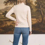 graced ivory knit long sleeve mock neck top worn by a woman with blonde hair in a bun, back view