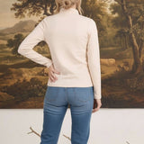 graced ivory knit long sleeve mock neck top worn by a woman with blonde hair in a bun, back view