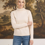 Model wearing a graced ivory knit long sleeve mock neck top paired with blue jeans in a studio setting