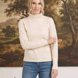 Model wearing a graced ivory knit long sleeve mock neck top paired with blue jeans in a studio setting