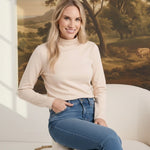 graced ivory knit long sleeve mock neck top worn by a blonde model sitting in a chair with blue jeans