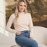 graced ivory knit long sleeve mock neck top worn by a blonde model sitting in a chair with blue jeans