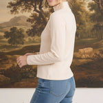 graced ivory long sleeve mock neck knit top worn by a blonde model against a landscape painting background