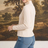 graced ivory long sleeve mock neck knit top worn by a blonde model against a landscape painting background
