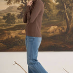 graced mocha knit long sleeve mock neck top worn by a woman with blue jeans and beige loafers in a studio setting