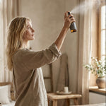 Woman in a bedroom holding a spray bottle, surrounded by natural light and decor.