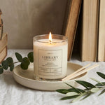 Candle labeled 'Library' with books and greenery on a neutral background
