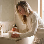 Woman in a bathroom setting with a candle and soap.