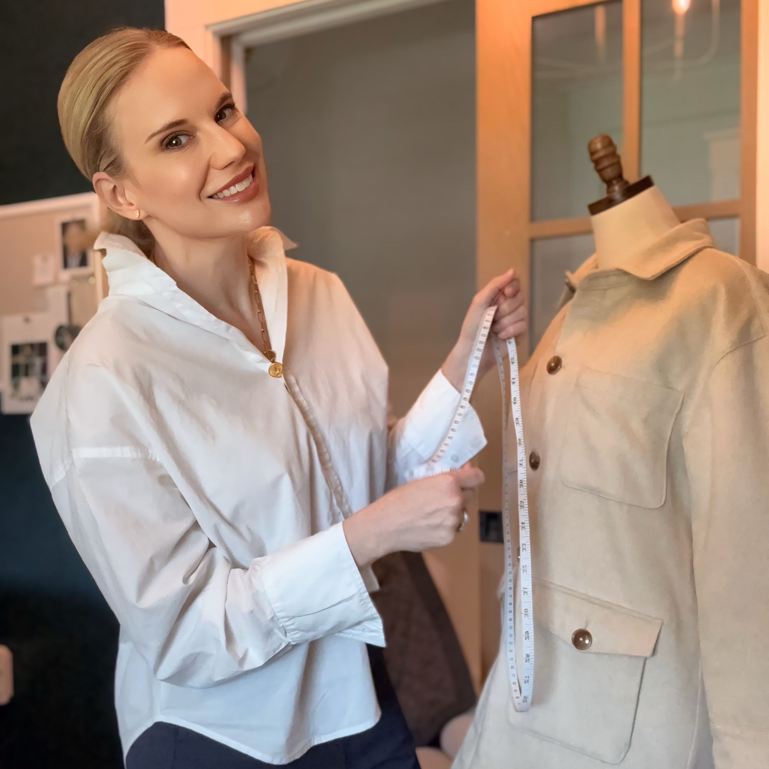 Woman measuring a beige jacket on a mannequin with a tape measure.