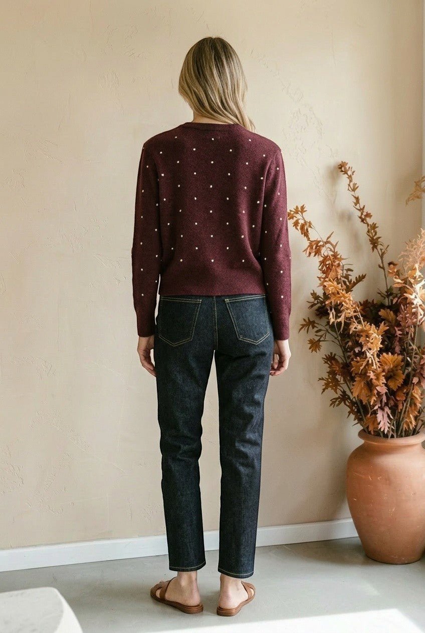 Woman wearing a graced burgundy cardigan with raised white polka dots, paired with dark denim jeans from behind.
