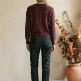 Woman wearing a graced burgundy cardigan with raised white polka dots, paired with dark denim jeans from behind.