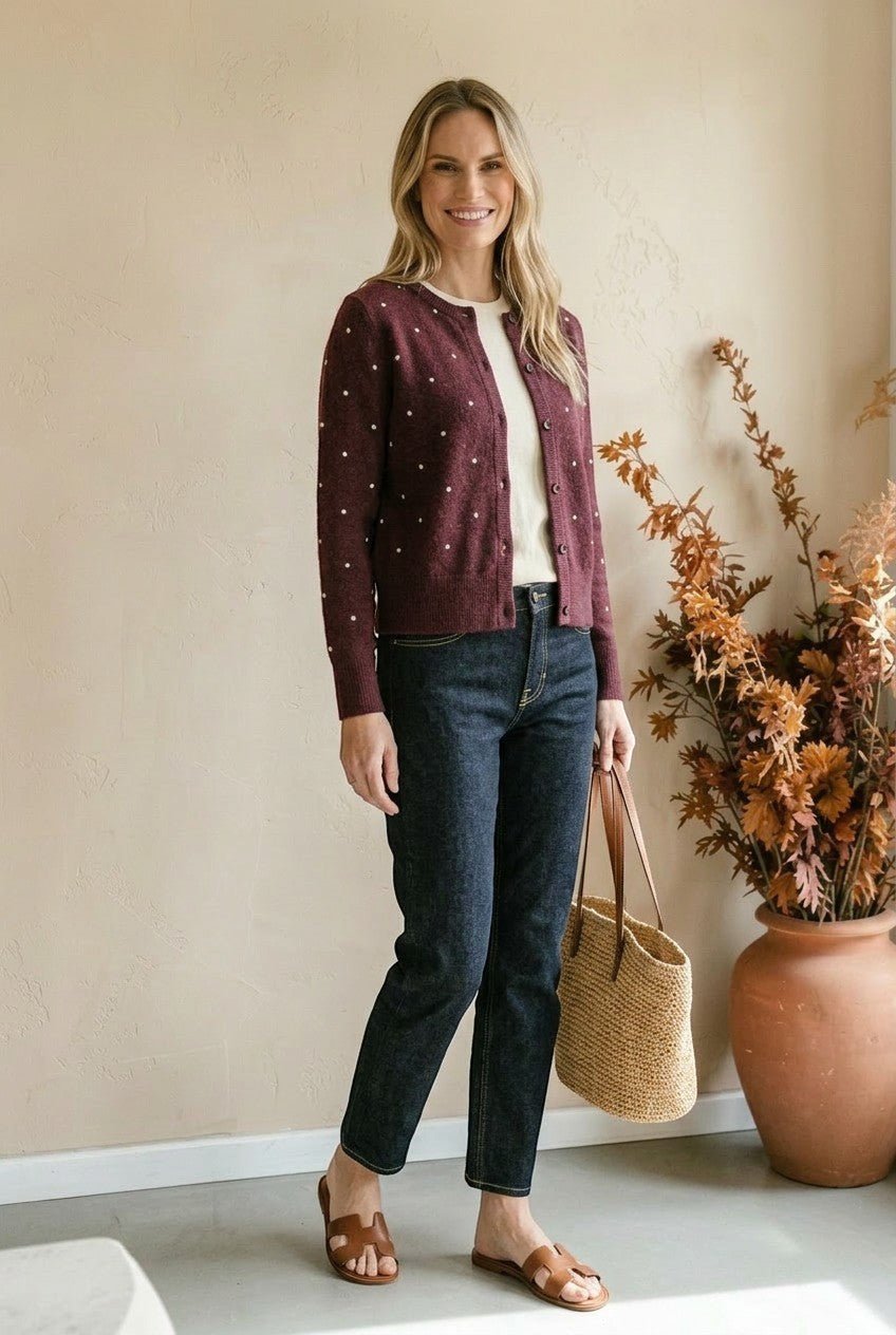 graced burgundy cardigan with raised white polka dots worn by a woman with dark jeans and a straw tote bag