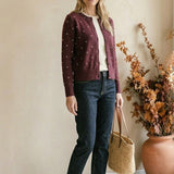 graced burgundy cardigan with raised white polka dots worn by a woman with dark jeans and a straw tote bag