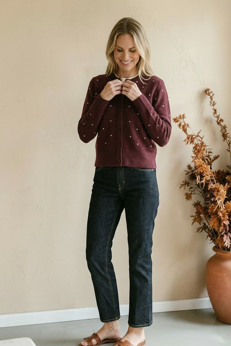Woman wearing a graced burgundy cardigan with raised white polka dots, paired with dark denim jeans.