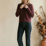 Woman wearing a graced burgundy cardigan with raised white polka dots, paired with dark denim jeans.