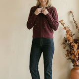 Woman wearing a graced burgundy cardigan with raised white polka dots, paired with dark denim jeans.