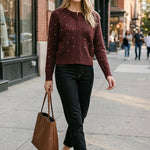 graced burgundy cardigan with raised polka dots worn by a smiling woman with a brown tote bag on a city sidewalk