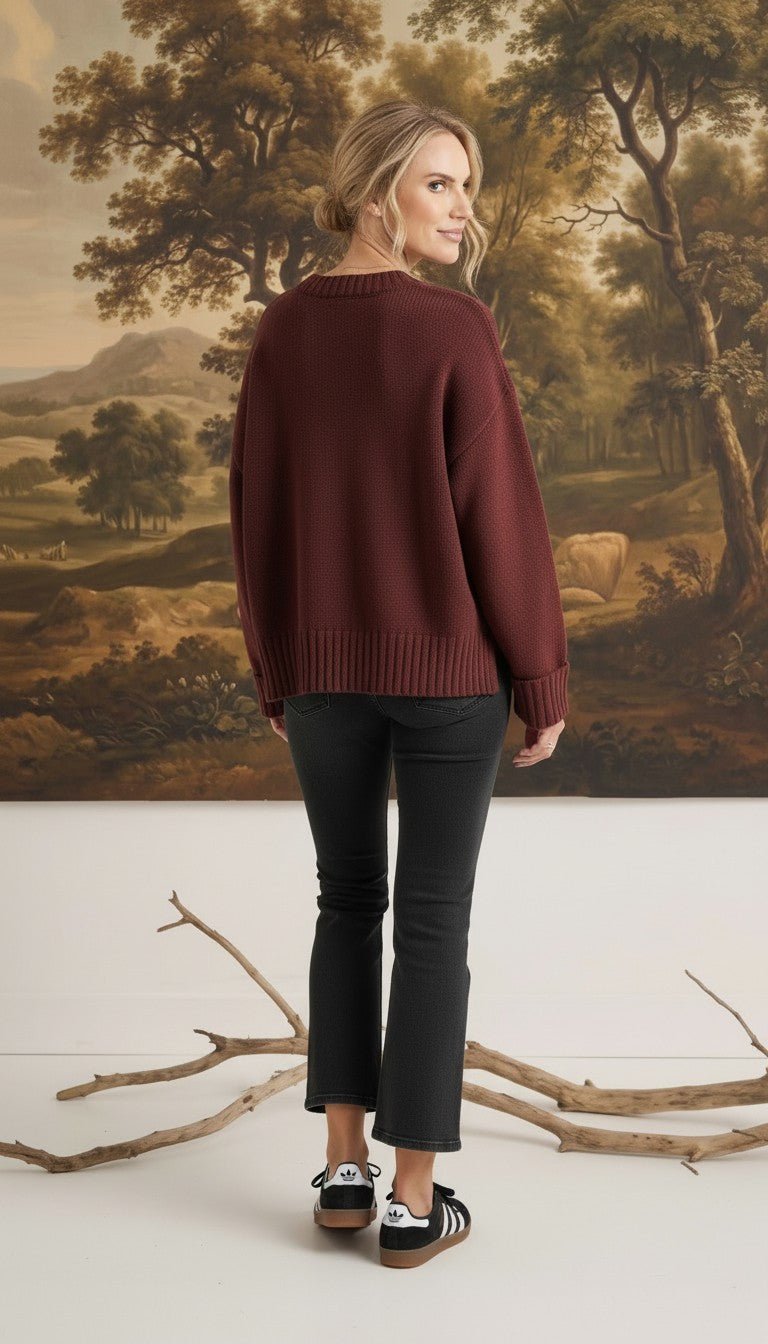 graced model wearing a cozy maroon ribbed cuff sweater with black jeans, back view against a landscape painting