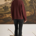 graced model wearing a cozy maroon ribbed cuff sweater with black jeans, back view against a landscape painting
