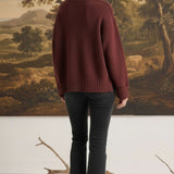 graced model wearing a cozy maroon ribbed cuff sweater with black jeans, back view against a landscape painting