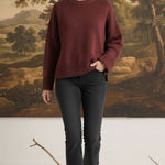 Model wearing a graced ribbed cuff sweater in deep coco brown with black jeans against a landscape mural background