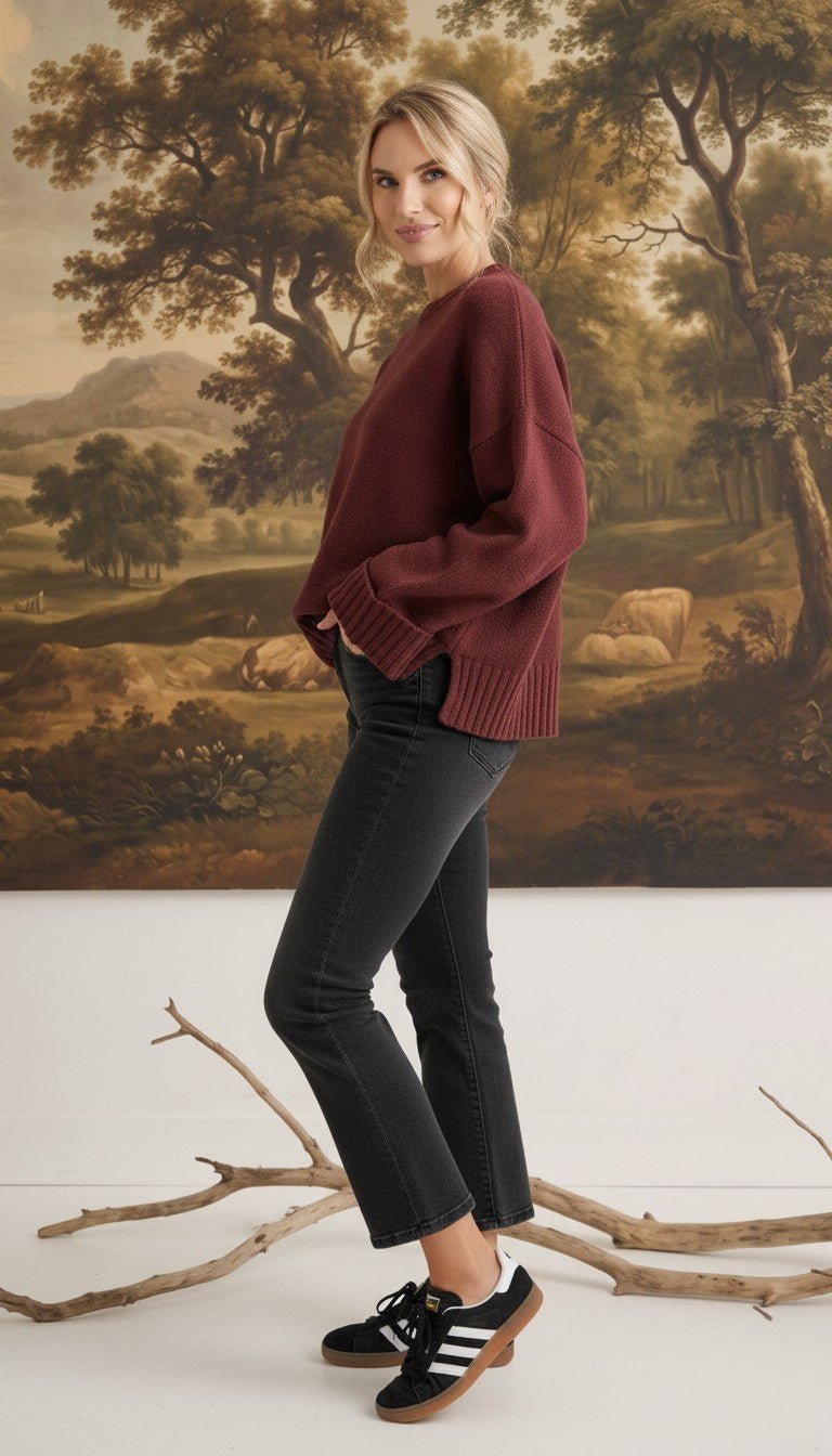 graced model wearing a cozy maroon ribbed cuff sweater with black jeans and sneakers against a landscape mural