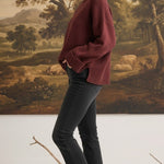 graced model wearing a cozy maroon ribbed cuff sweater with black jeans and sneakers against a landscape mural
