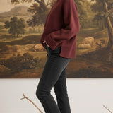 graced model wearing a cozy maroon ribbed cuff sweater with black jeans and sneakers against a landscape mural