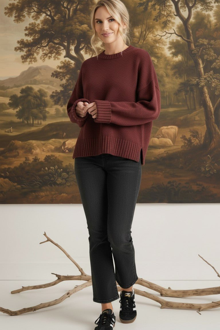 Model wearing a graced maroon ribbed cuff sweater with a relaxed fit, paired with black jeans in a studio setting.
