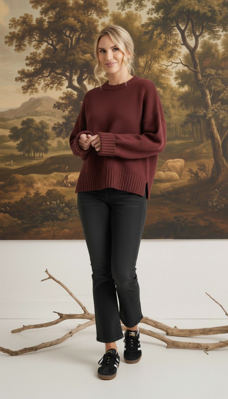 Model wearing a graced maroon ribbed cuff sweater with a relaxed fit, paired with black jeans in a studio setting.