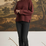 Model wearing a graced maroon ribbed cuff sweater with a relaxed fit, paired with black jeans in a studio setting.