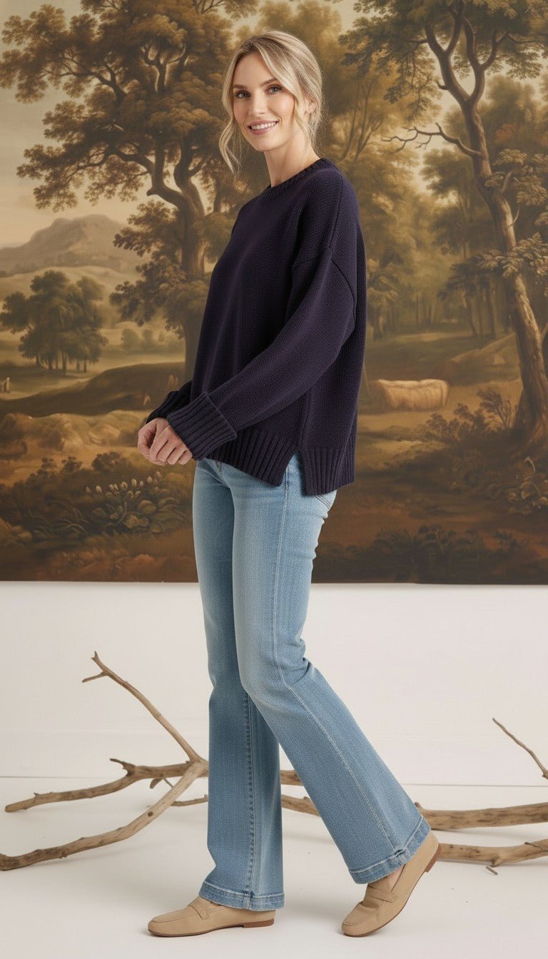Model wearing a graced navy ribbed cuff sweater with light wash flared jeans and tan loafers in a studio setting