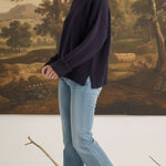 Model wearing a graced navy ribbed cuff sweater with light wash flared jeans and tan loafers in a studio setting