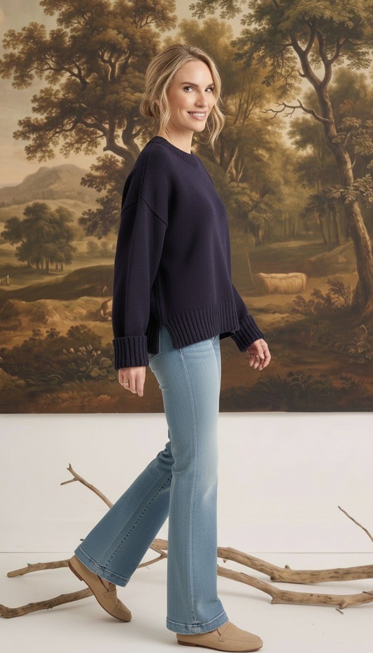 Model wearing a graced navy ribbed cuff sweater with a relaxed fit, paired with light blue flare jeans and loafers.