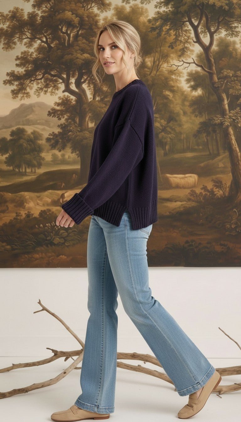 Model wearing a graced navy blue cotton-blend sweater with ribbed cuffs and a relaxed fit, paired with flared jeans.