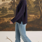 Model wearing a graced navy blue cotton-blend sweater with ribbed cuffs and a relaxed fit, paired with flared jeans.