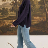Model wearing a graced navy blue cotton-blend sweater with ribbed cuffs and a relaxed fit, paired with flared jeans.