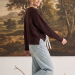 A woman wearing a graced brown crew neck sweater with ribbed cuffs and hem, styled with light wash jeans.