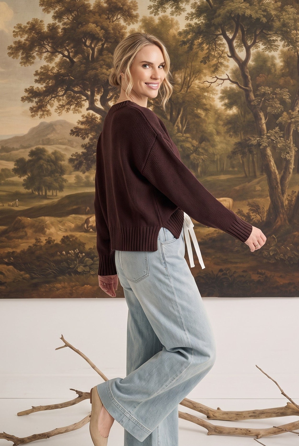 A woman wearing a graced brown crew neck sweater with ribbed cuffs and hem, styled with light wash jeans.