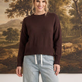 A woman wearing a brown graced crew neck sweater with ribbed detailing, paired with light wash wide-leg jeans.