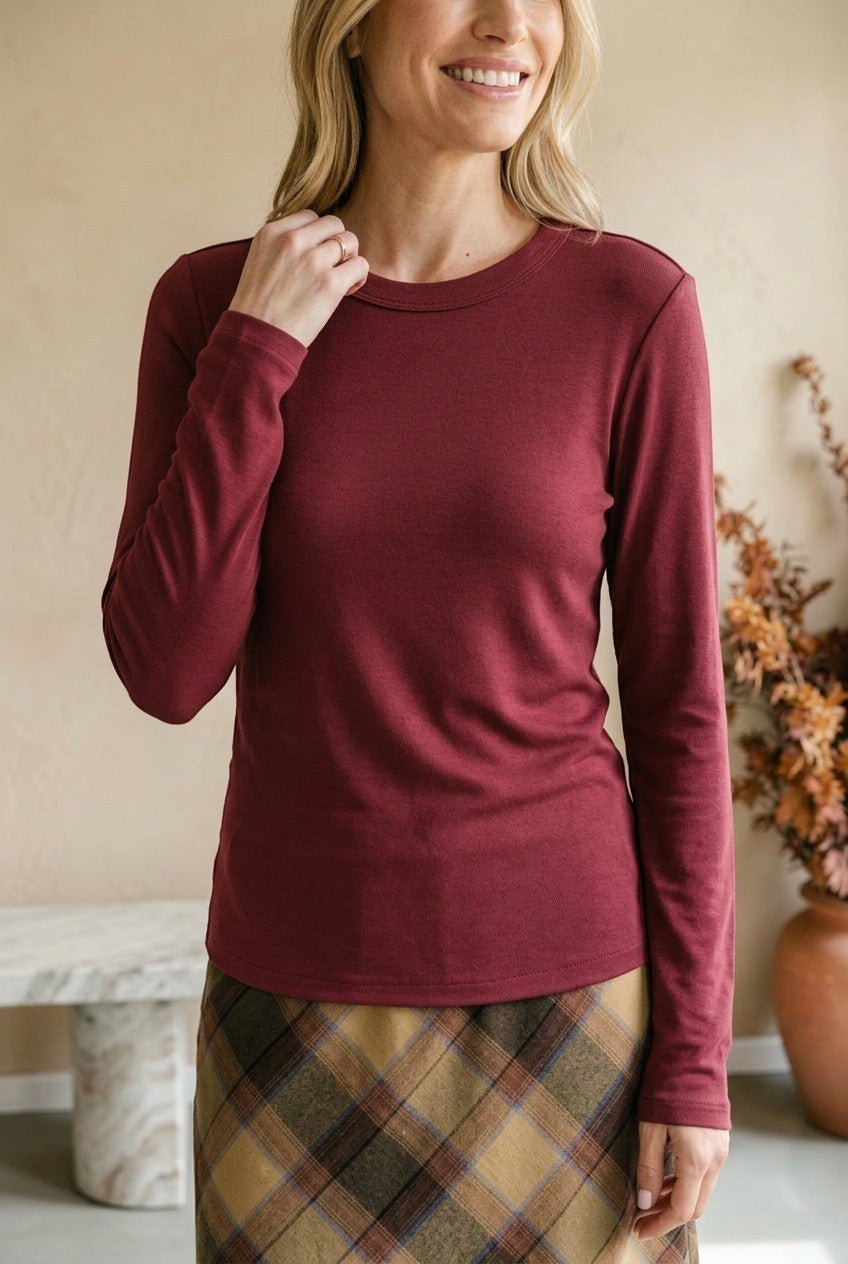 A woman wearing a graced wine-colored long-sleeve round neck knit top with a fitted silhouette.