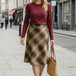 graced wine round neck knit top worn by a woman with a plaid midi skirt and straw tote bag on a city street