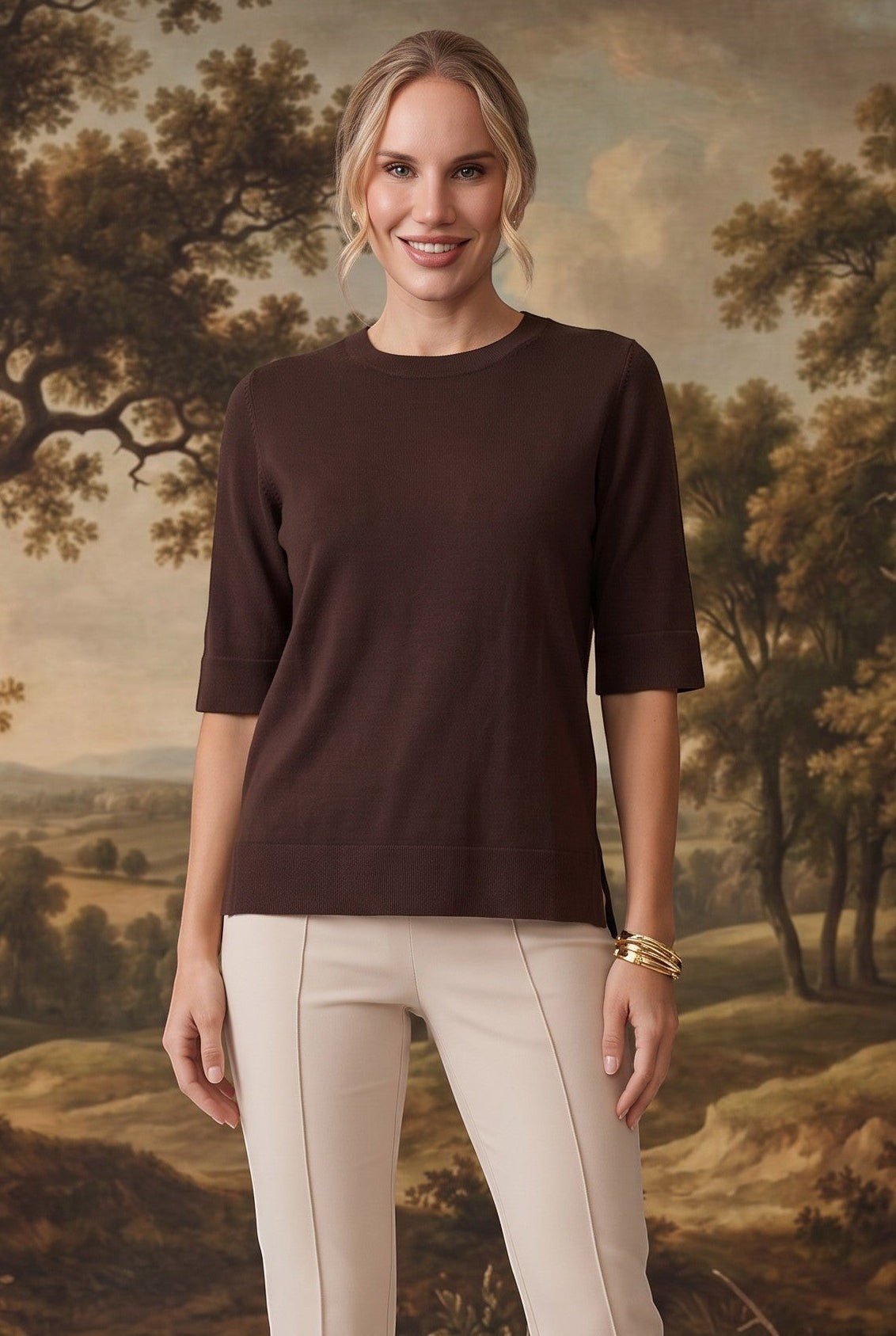 graced espresso brown short sleeve knit top worn by a model with beige trousers against a scenic landscape backdrop